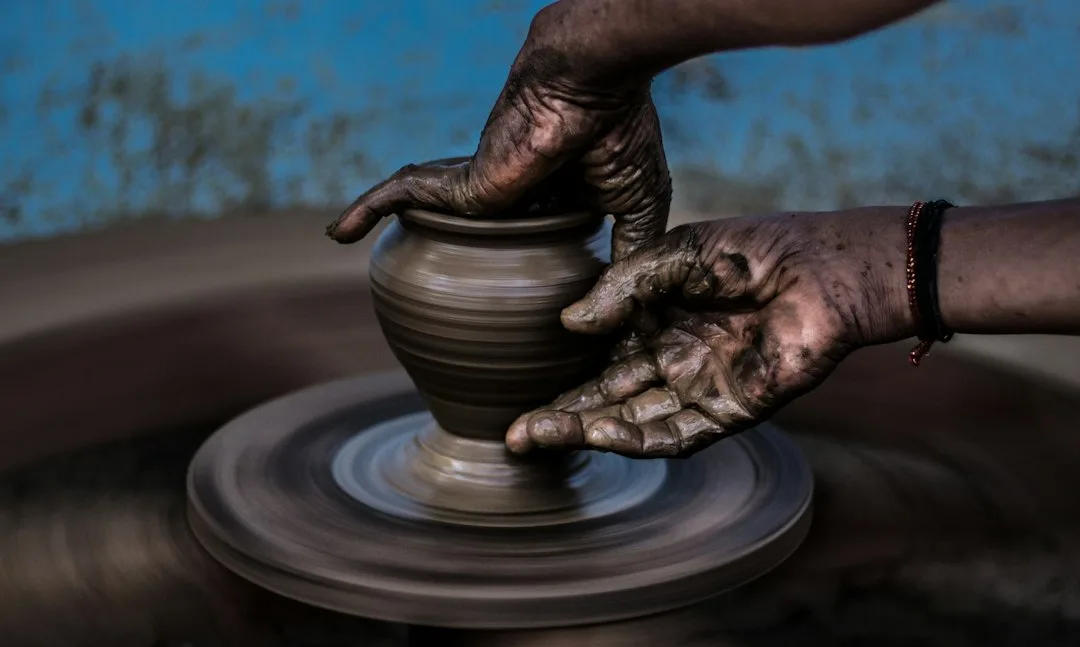 A pair of clay-covered hands shaping a bowl on a spinning pottery wheel
